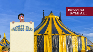Blau-gelb-gestreiftes Zirkuszelt mit Clown im Vordergrund und Plakat mit Aufschrift Manege frei